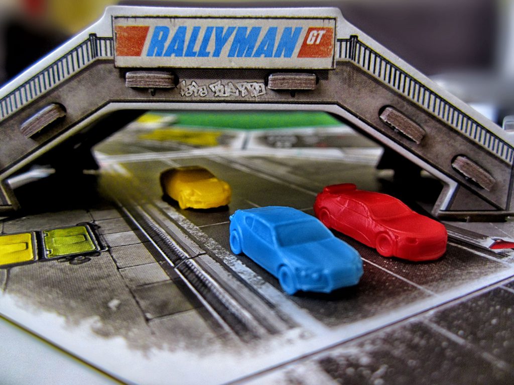 Rallyman: GT board game, featuring cars racing on a track as they pass under an overpass.