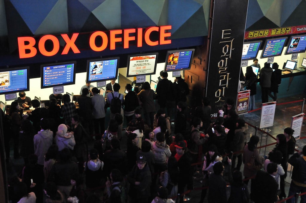 Long lines of people queue in front of a Box Office.