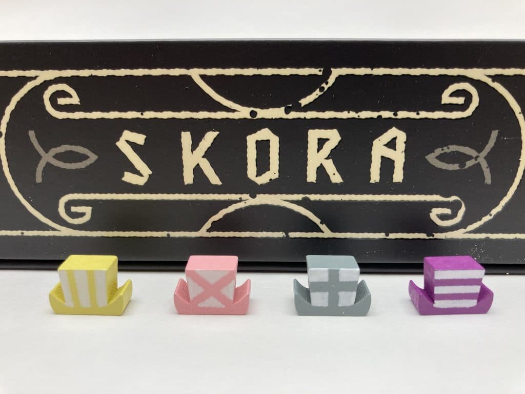 Skora Board Game Boats lined up, a yellow with vertical lines on the sail, pink with an X on the sail, gray with a cross on the sail, and purple with horizontal stripes on the sail.