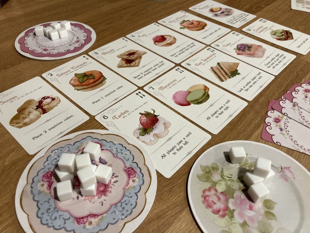 Elevenses: The Guilty Party board game with up-turned spread, and plates with sugar cubes